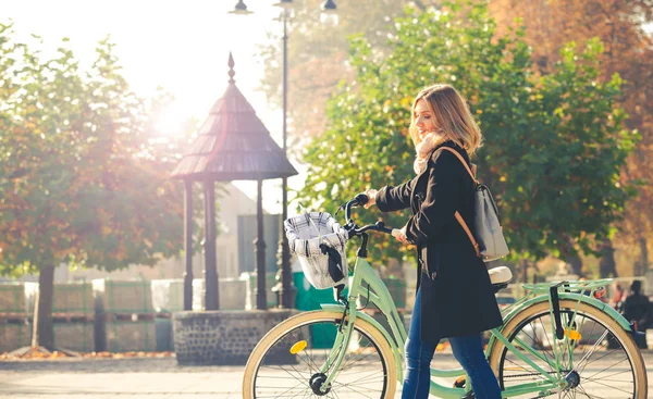 Ragazza in cappotto con bici retrò sulla strada d'autunno — Foto Stock