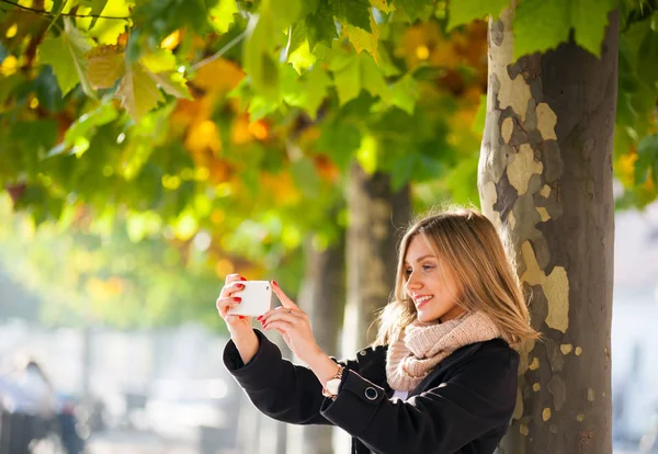 Девушка фотографируется с мобильного телефона осенью в городе — стоковое фото