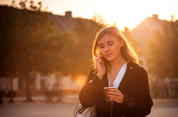 Woman talking on the phone and walking at the city street during sunset — Stock Photo, Image