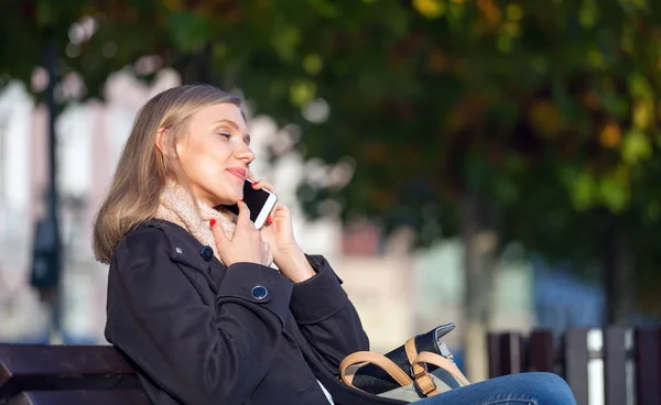 Meisje met mobiele telefoon buiten zitten op bankje op de straat — Stockfoto