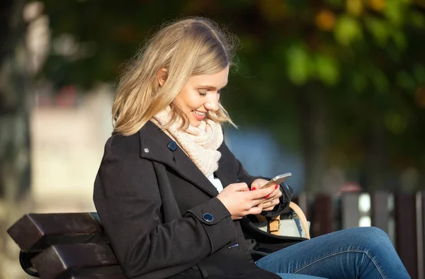 Menina usando telefone celular ao ar livre sentado no banco na rua — Fotografia de Stock