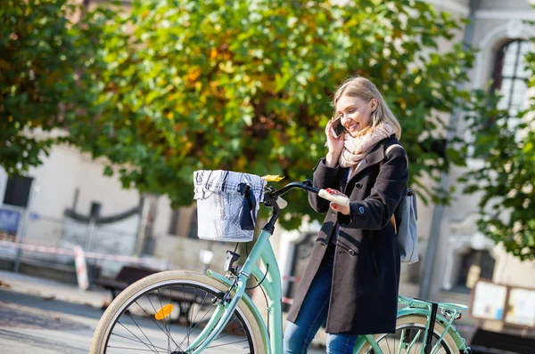 Vrouw met behulp van de telefoon tijdens het wandelen in de stad met de fiets — Stockfoto