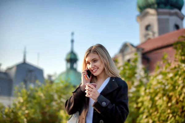 Girl with coffee cup talking on the phone and walking at the street — Stock Photo, Image