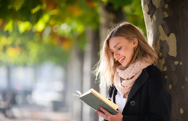 Mladá žena s knihou venkovní pod barevné podzimní stromy na náměstí — Stock fotografie