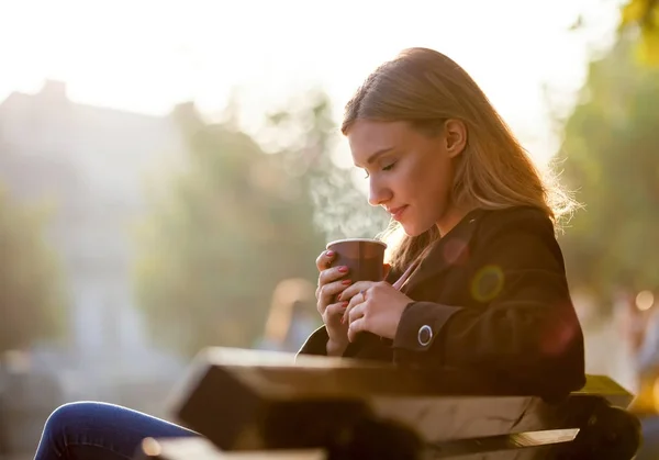 Femeia care miroase și bea cafea fierbinte, apusul de toamnă pe stradă — Fotografie, imagine de stoc