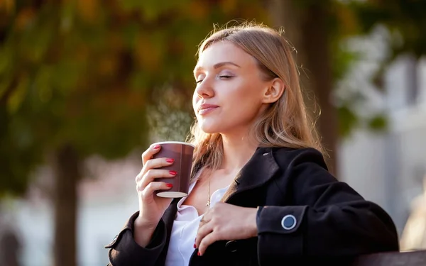 महिला गर्म कॉफी की सुगंध और पी रही है, सड़क पर शरद ऋतु सूर्यास्त — स्टॉक फ़ोटो, इमेज