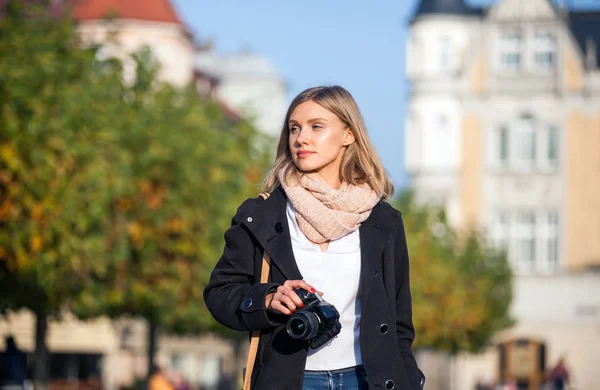 Girl with camera walking in the city street and looking at something — Stock Photo, Image