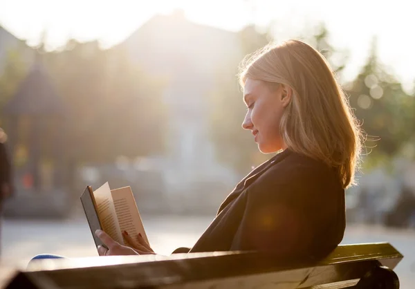 Mladá dívka čtení kniha při západu slunce na náměstí — Stock fotografie