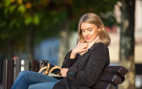 Młoda kobieta siedzi na ławce na ulicy podczas słoneczny jesienny dzień miasta — Zdjęcie stockowe