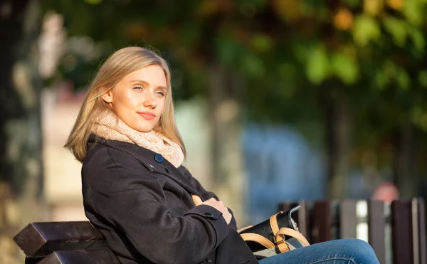 Young woman sitting on bench at the city street during sunny autumn day
