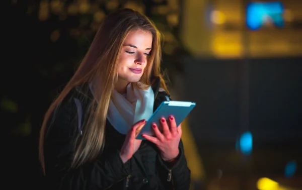 Hermosa mujer usando tableta en la ciudad por la noche —  Fotos de Stock
