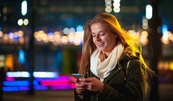 Mujer usando teléfono móvil por la noche en la ciudad entre luces de neón —  Fotos de Stock