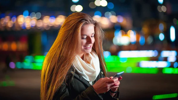 Mujer usando teléfono móvil por la noche en la ciudad entre luces de neón —  Fotos de Stock