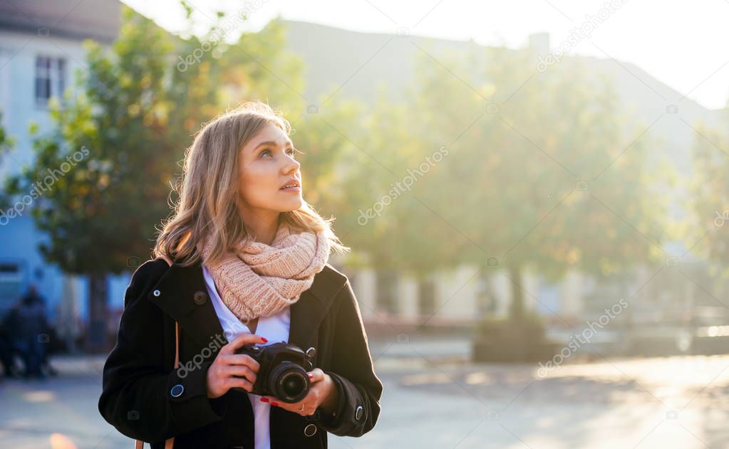 Girl with camera walking in the city street and looking at something