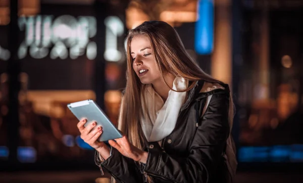 Chica en la ciudad por la noche usando tableta sentada en el banco —  Fotos de Stock