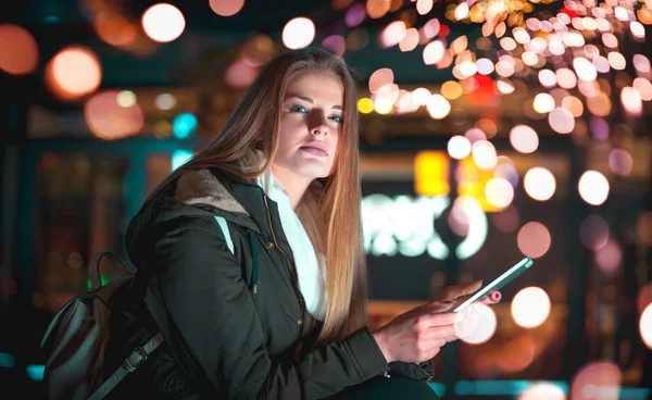 Menina na cidade à noite usando tablet sentado no banco — Fotografia de Stock