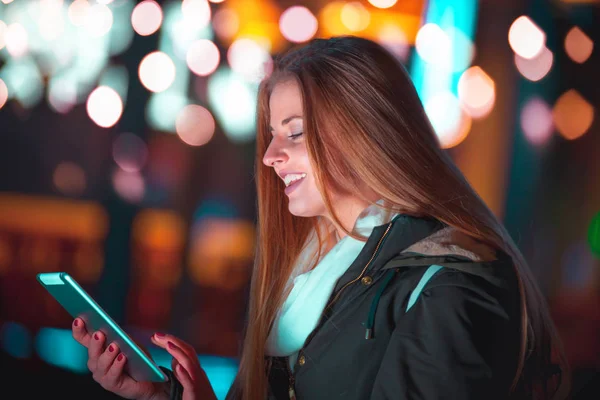 Девушка в городе ночью с помощью планшета сидит на скамейке — стоковое фото