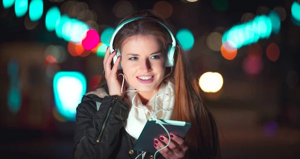 Vrouw met hoofdtelefoon met behulp van de Tablet PC en luisteren van muziek in de stad bij nacht — Stockfoto