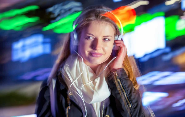 Woman with headphones in the city at night among neon moving lights, fashion portrait — Stock Photo, Image