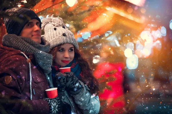 Mercado de Natal nevado, Casal com bebidas quentes se divertindo — Fotografia de Stock