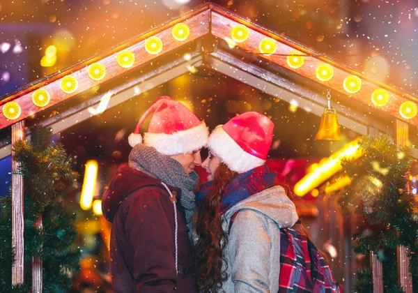 Couple in warm clothes hugging at Christmas market with snowfall — Stock Photo, Image