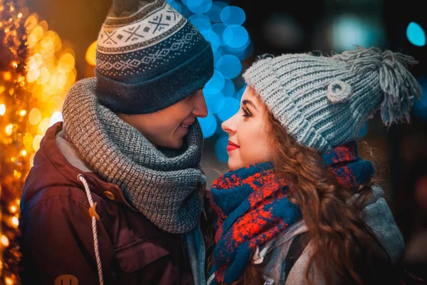 Любящая пара на фоне рождественских огней во время вечерней прогулки по городу — стоковое фото