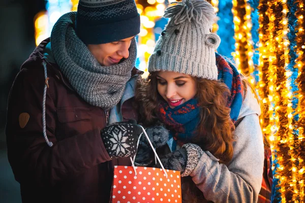 Casal com saco de presente no fundo luzes de Natal, andando na cidade à noite — Fotografia de Stock