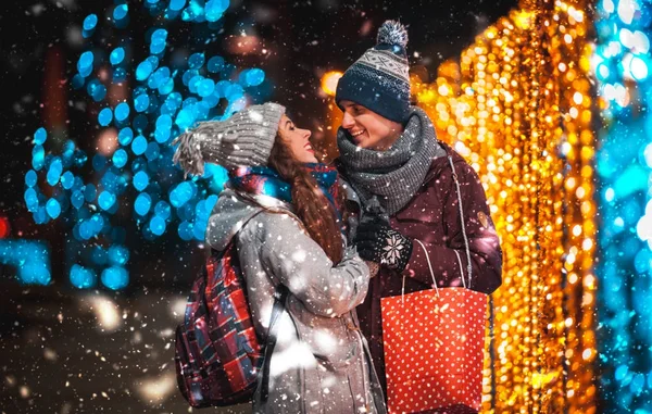 Paar mit Geschenktüte auf Weihnachtsbeleuchtung Hintergrund, Spaziergang in der Stadt am Abend — Stockfoto