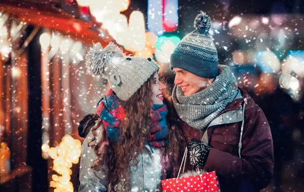 Молодая пара веселится на рождественской ярмарке со снегопадом — стоковое фото