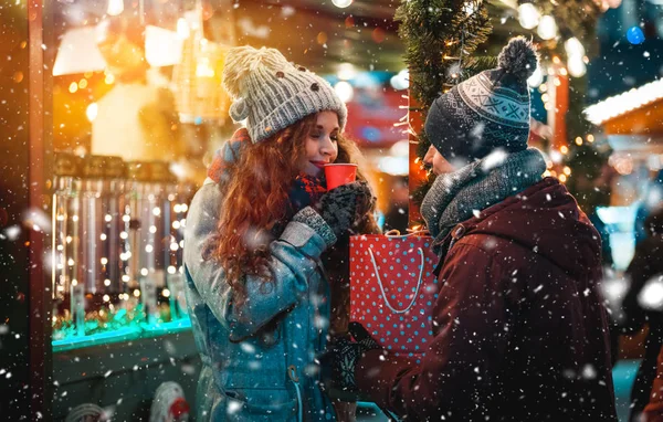 Vánoční trh restaurace na večer s sněžení, pár s horké nápoje v pohádkové prostředí — Stock fotografie