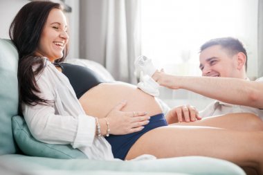 Hamile çift evde koltukta oturan Bebek Patiği birlikte oynarken