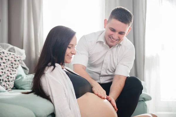 Junges schwangeres Paar entspannt sich zu Hause, berührt Bauch — Stockfoto