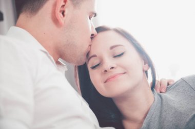 Güzel çift öpüşme ve evde güneş ışığı ile pencere yakınındaki sarılma