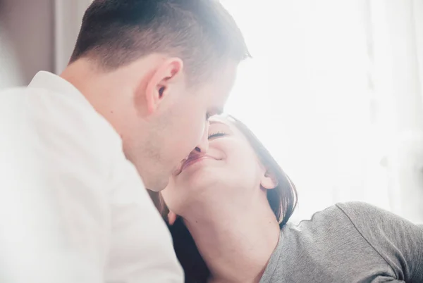 Belo casal beijando e abraçando em casa perto da janela com luz solar — Fotografia de Stock