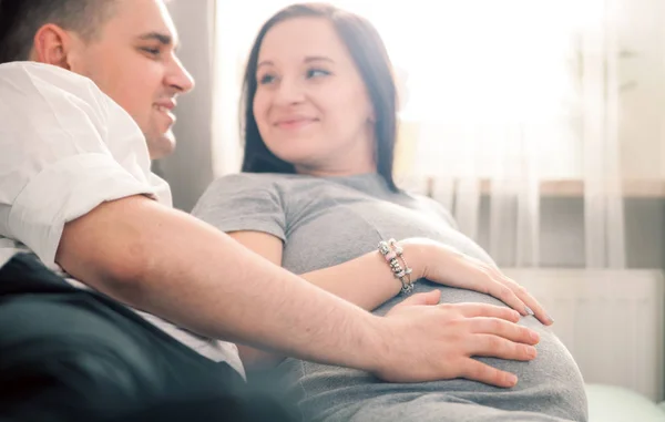 Junges schwangere Paar entspannt auf Sofa zu Hause, Bauch anfassen — Stockfoto