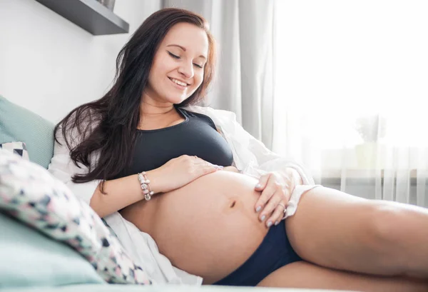Расслабленная, улыбающаяся беременная женщина лежит дома на диване — стоковое фото
