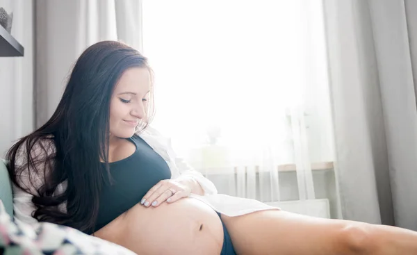 Расслабленная, улыбающаяся беременная женщина лежит на диване и отдыхает дома. — стоковое фото