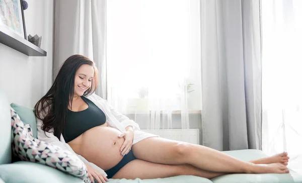 Расслабленная, улыбающаяся беременная женщина лежит на диване и отдыхает дома. — стоковое фото