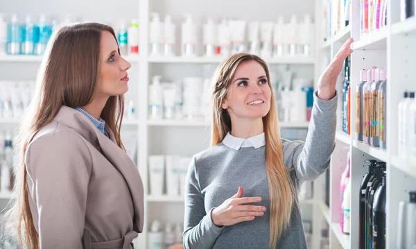 Mujer cliente elegir cosméticos con asistente en la tienda de belleza —  Fotos de Stock