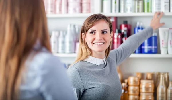 Mujer cliente elegir cosméticos con asistente en la tienda de belleza —  Fotos de Stock