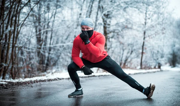 Winter running exercise, runner stretching on road in snowy forest