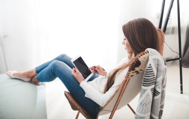 Kadın evde modern sandalyede oturan ve tablet bilgisayar, oturma odasında rahatlatıcı kullanıyor