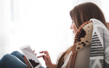 Kadın evde modern sandalyede oturan ve tablet bilgisayar, oturma odasında rahatlatıcı kullanıyor