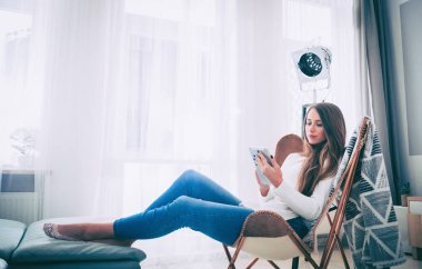 Kadın evde modern sandalyede oturan ve tablet bilgisayar, oturma odasında rahatlatıcı kullanıyor