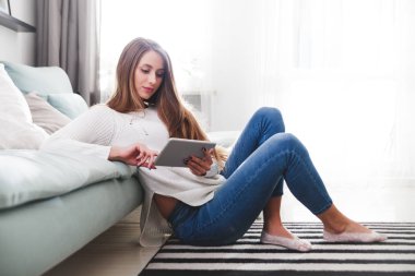 Kadın evde halı üzerinde oturan ve tablet bilgisayar kullanarak