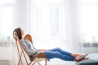Kadın evde pencere oturma odasında rahatlatıcı yakın modern sandalyede oturan