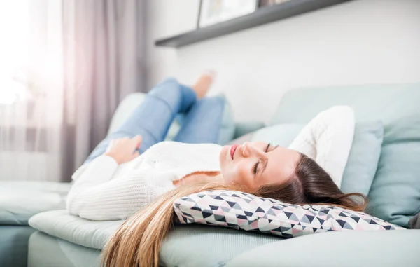 En lykkelig kvinne som slapper av og ligger på sofaen hjemme – stockfoto