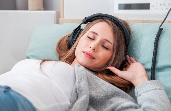 Young woman with headphones lying on floor listening to music at home in living room