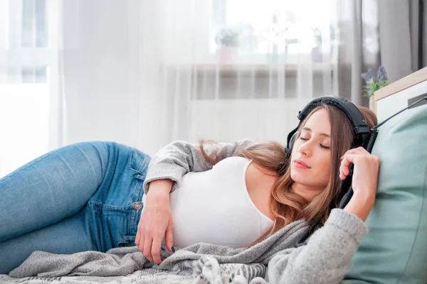 Молодая женщина в наушниках лежит на полу, слушая музыку в — стоковое фото
