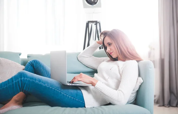 Mujer segura en casa acostada en el sofá y trabajando con el ordenador portátil —  Fotos de Stock